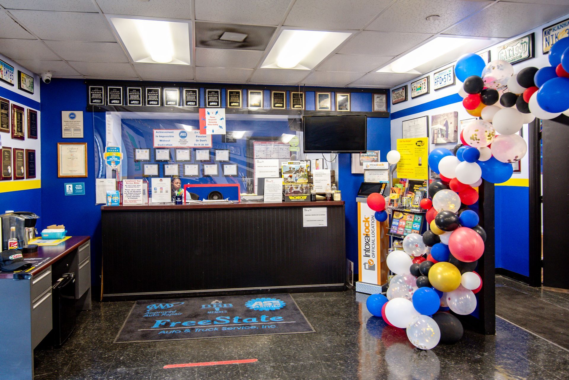 Reception area of a business; blue walls, dark counter, balloons, framed certificates, waiting area | Freestate Auto & Truck Service