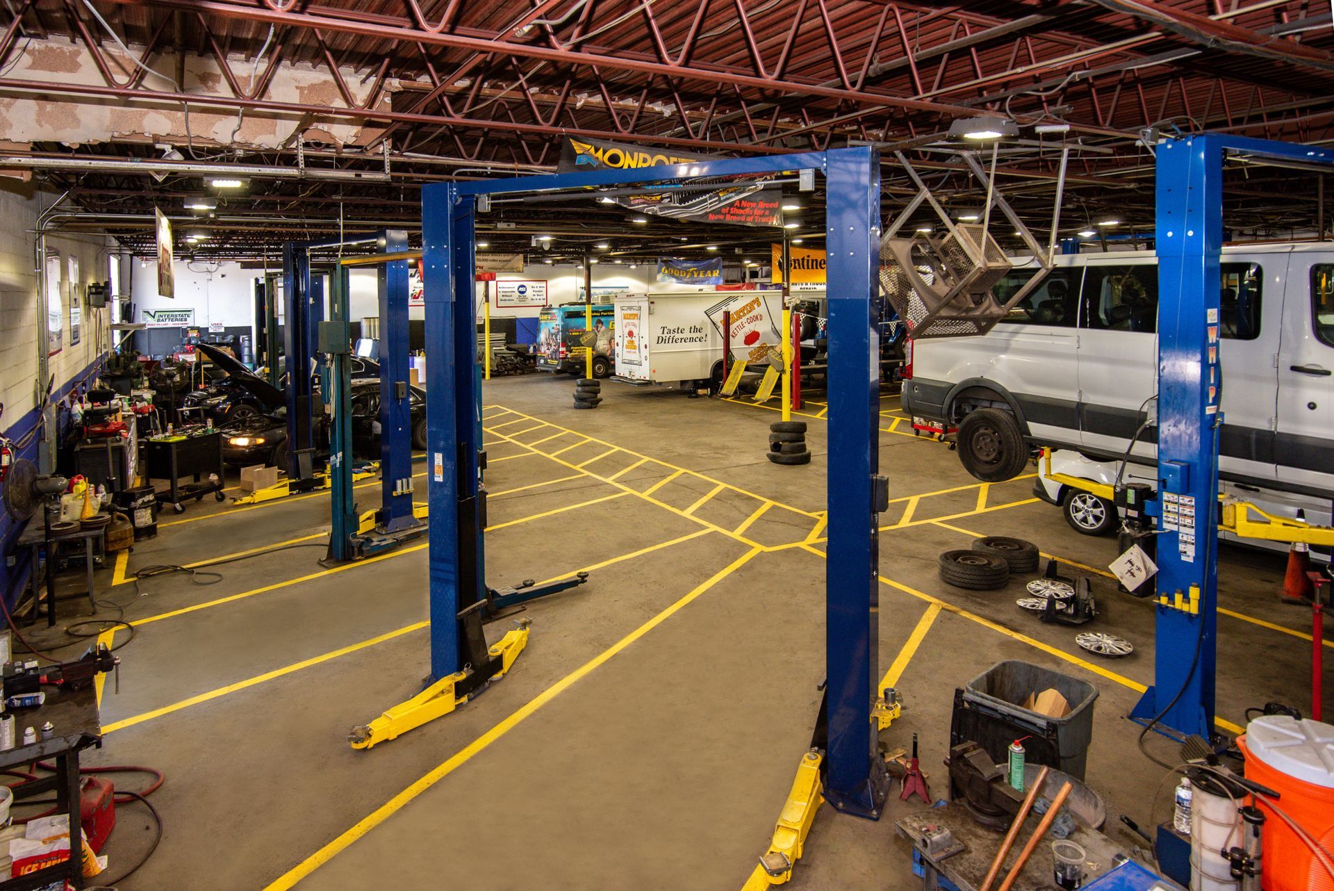 Garage with multiple vehicle lifts, a white van, and various tools on the floor. Yellow floor lines | Freestate Auto & Truck Service