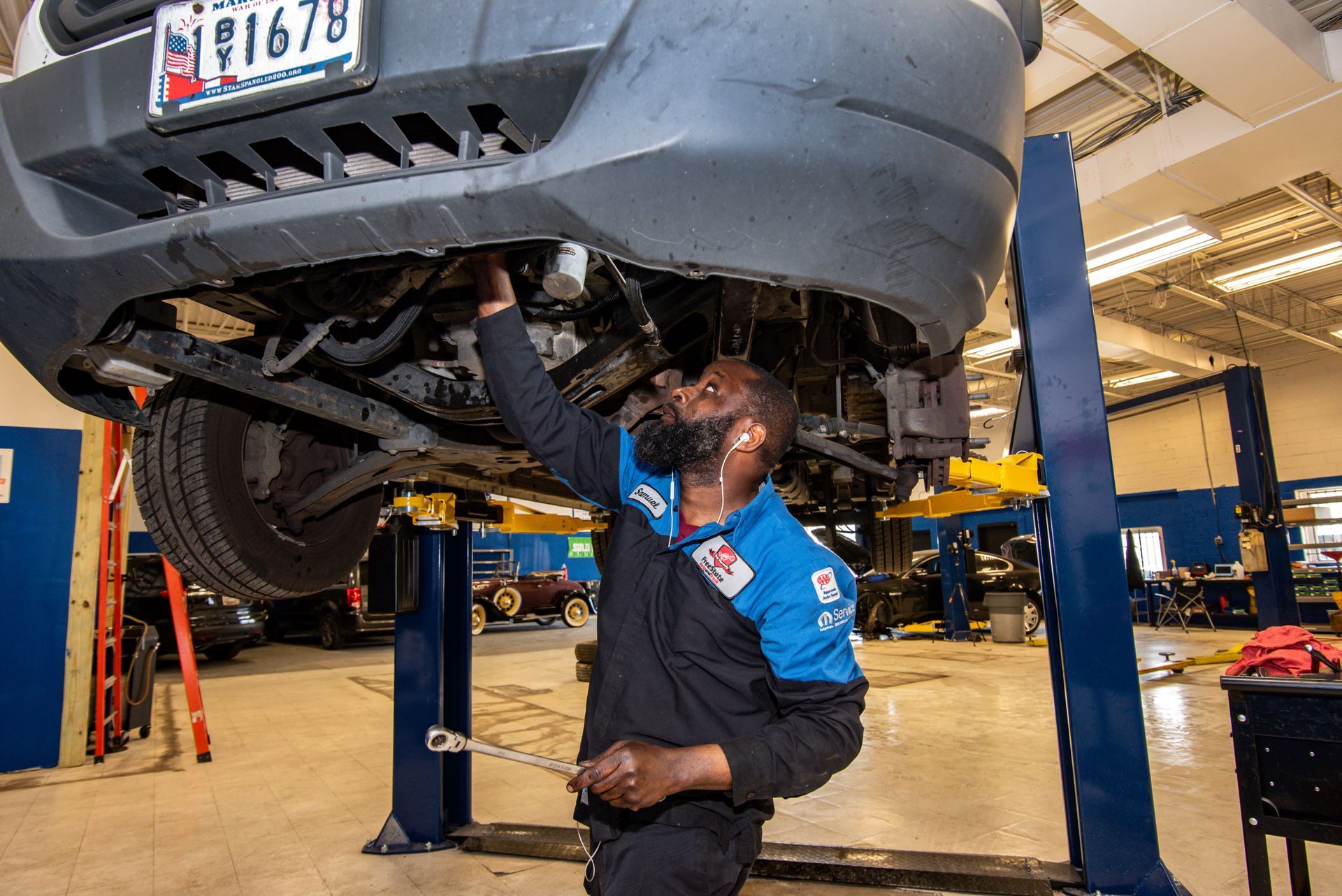 Mechanic under a raised vehicle, using a wrench. Garage setting with a lift | Freestate Auto & Truck Service