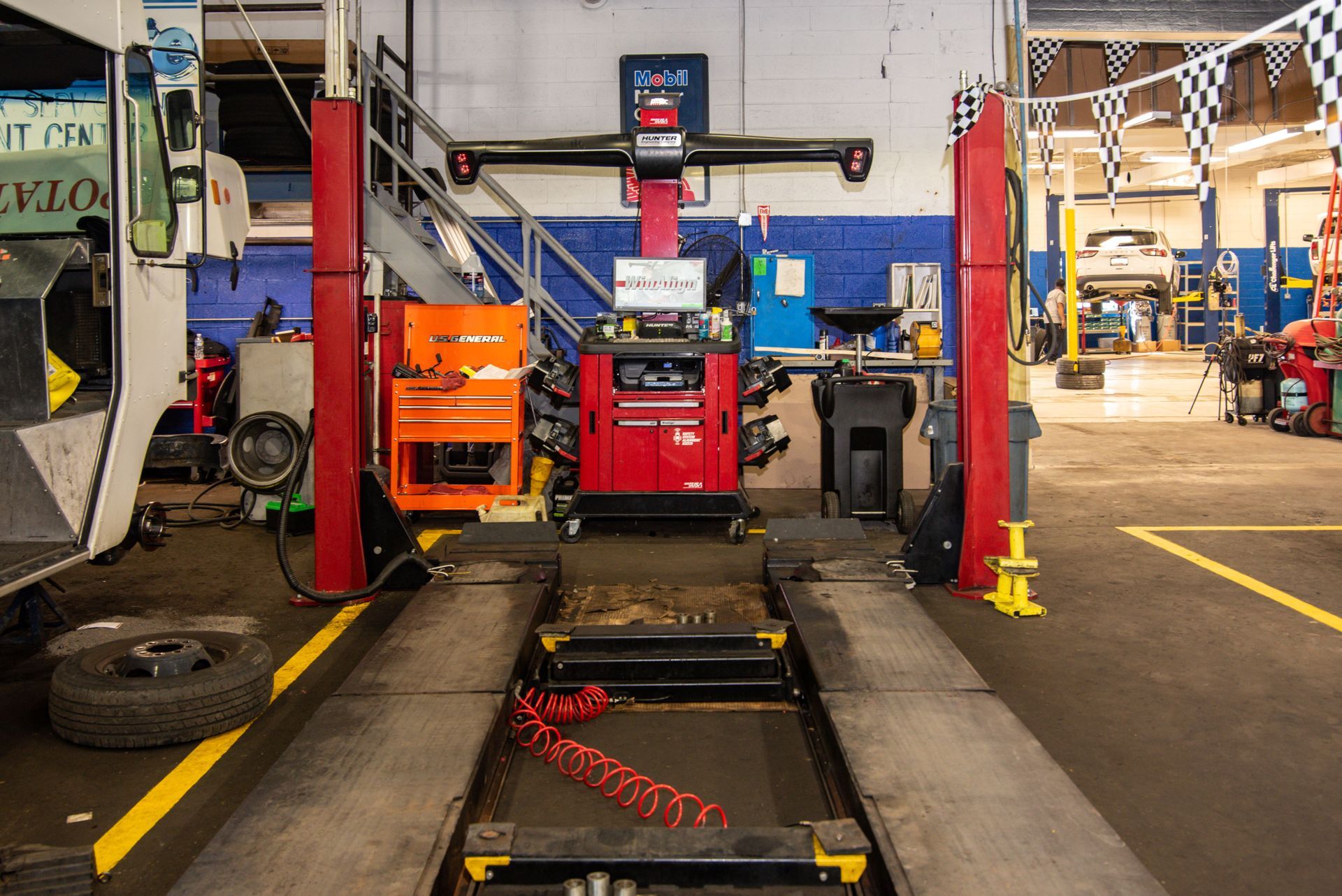 An automotive shop interior with a wheel alignment machine. Red, orange, and blue tools are visible with a car up on a lift in the background | Freestate Auto & Truck Service
