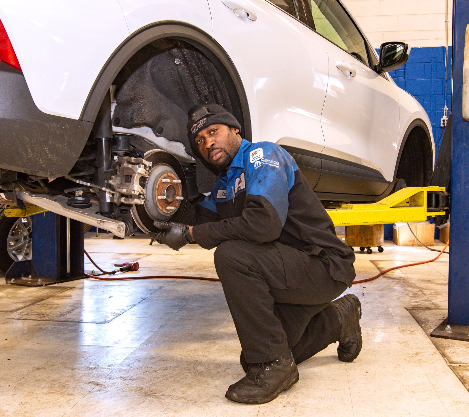 Mechanic working on car's brakes in a shop. The car is on a lift. Mechanic kneels, looking at camera | Freestate Auto & Truck Service