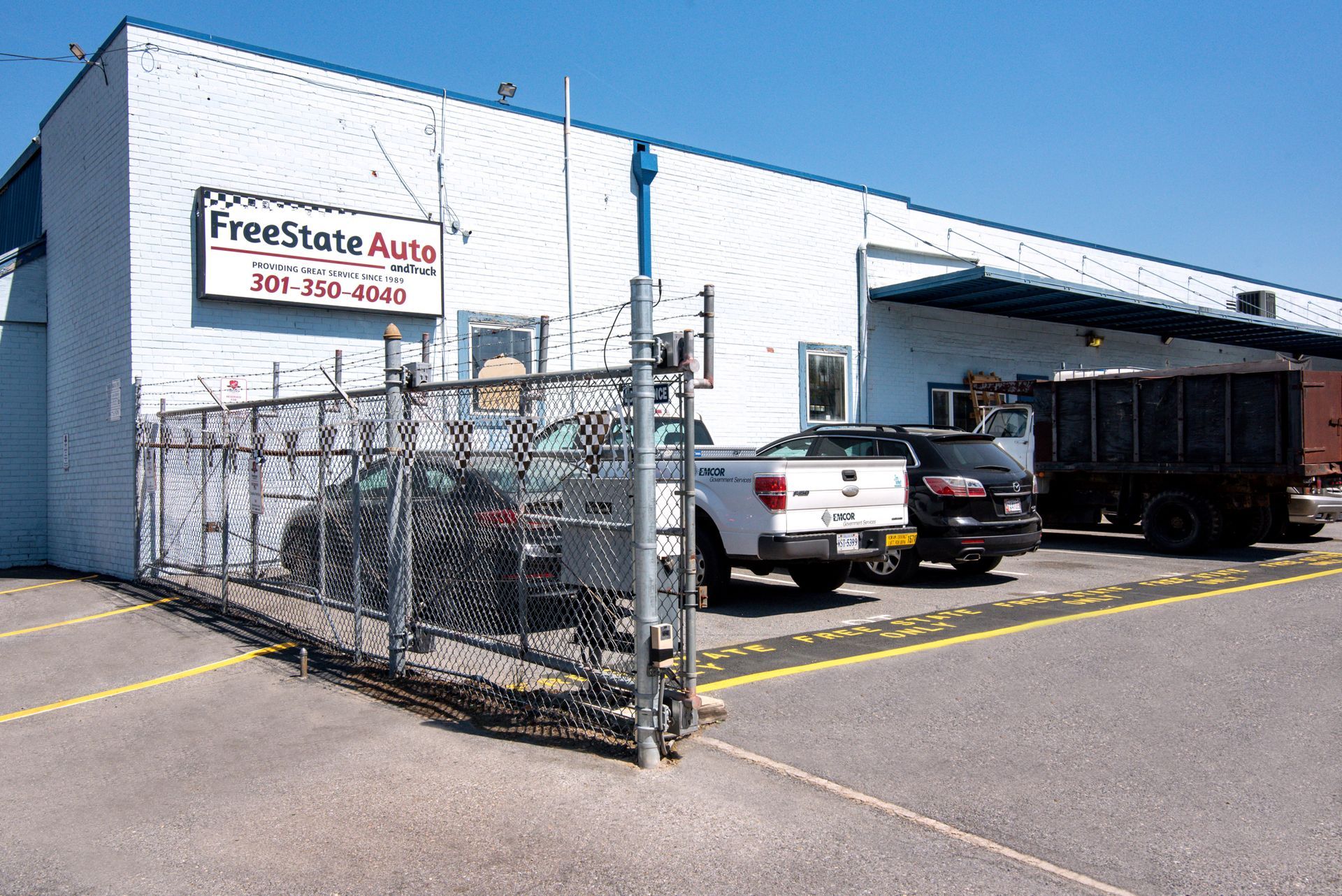 FreeState Auto building with vehicles parked in front behind a chain-link fence | Freestate Auto & Truck Service
