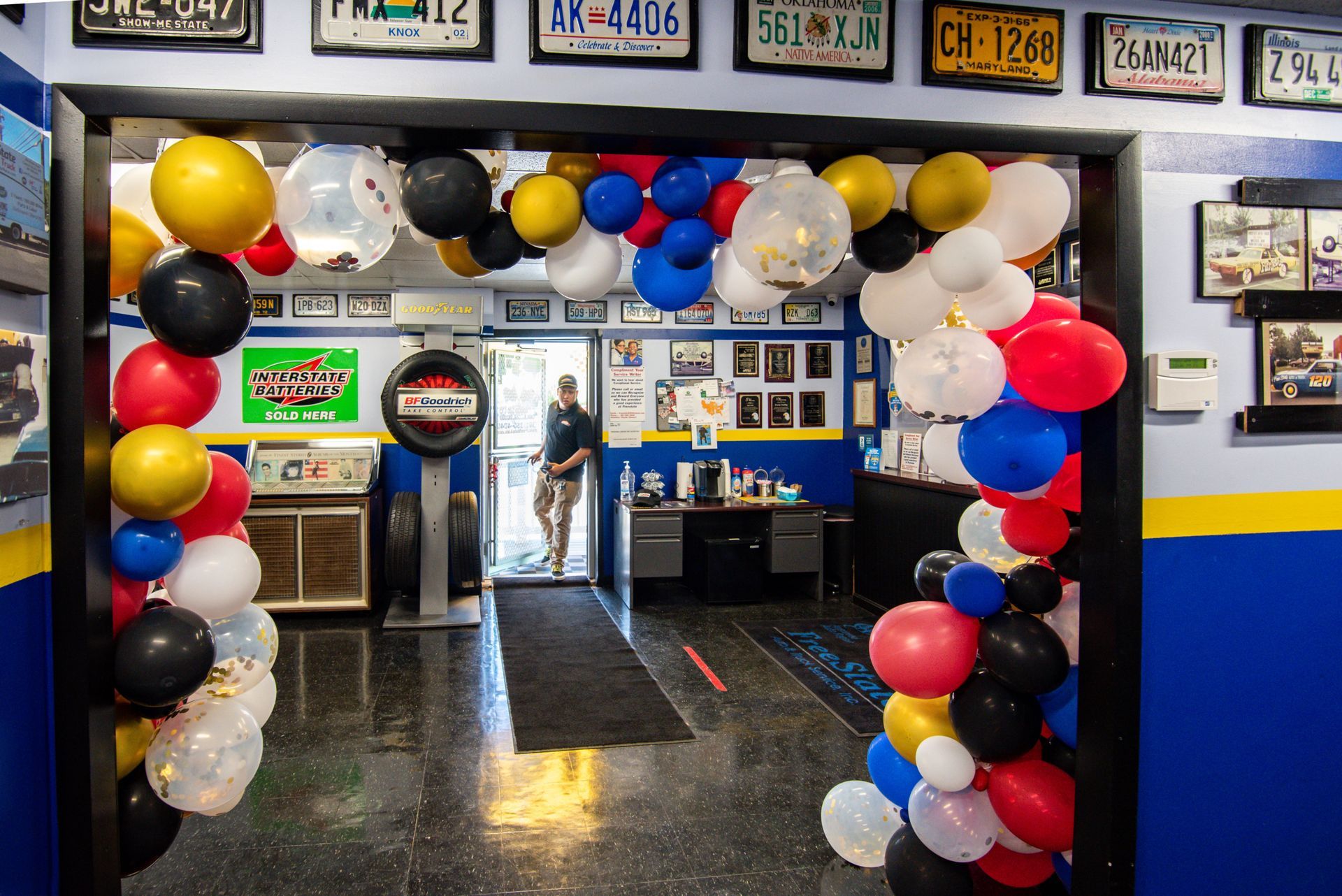 Entrance to a business decorated with balloons, license plates above. A person stands inside the doorway | Freestate Auto & Truck Service