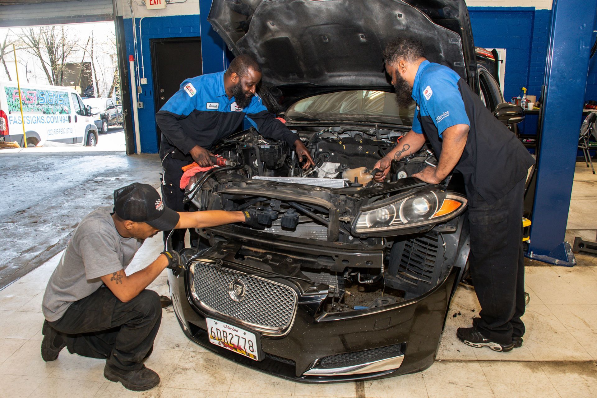 Three mechanics working on the engine of a car inside a repair shop. One kneels, two stand, all looking at the car | Freestate Auto & Truck Service