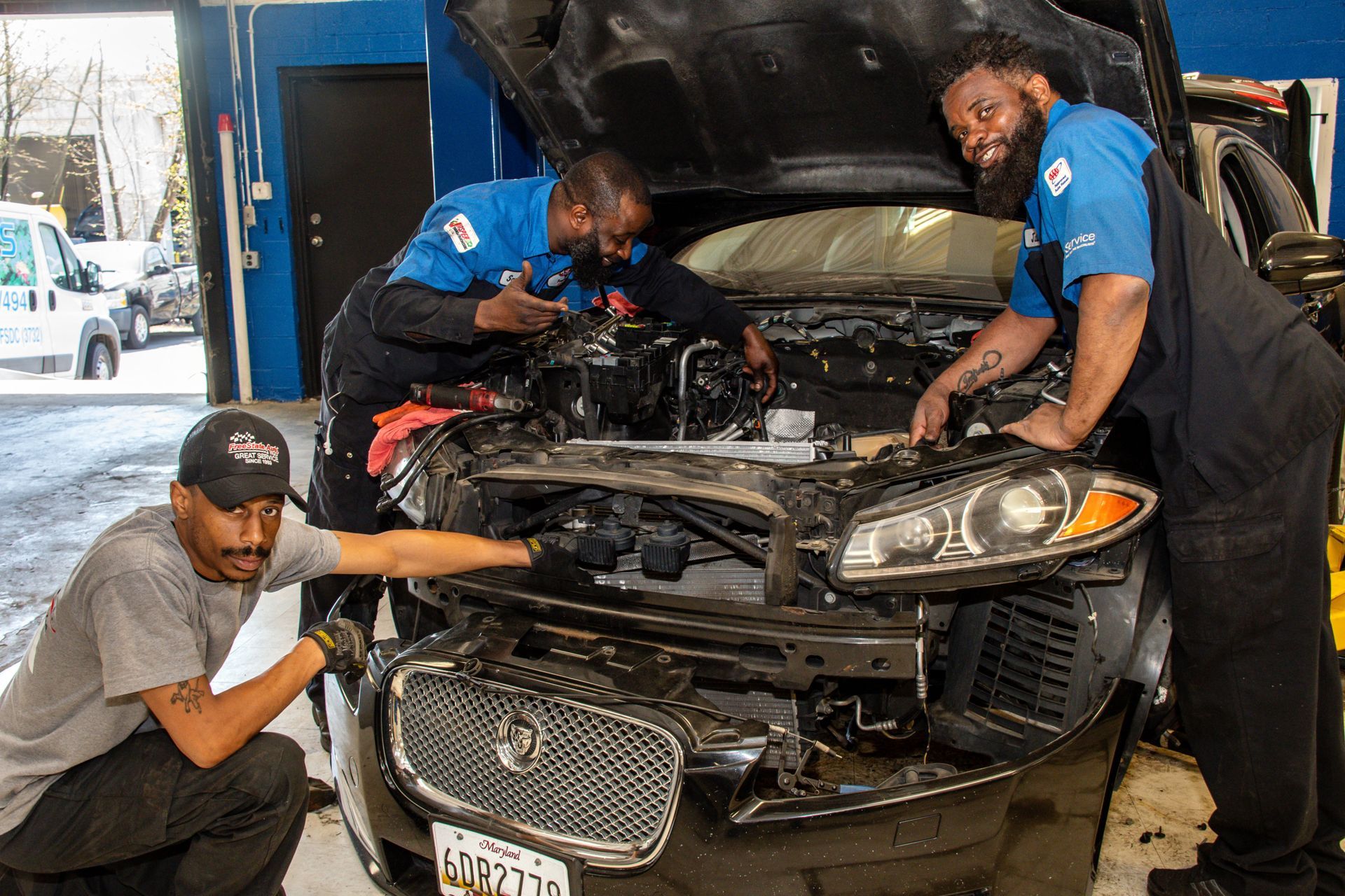Three auto mechanics working on a car in a shop, one pointing at the front, others under the hood | Freestate Auto & Truck Service
