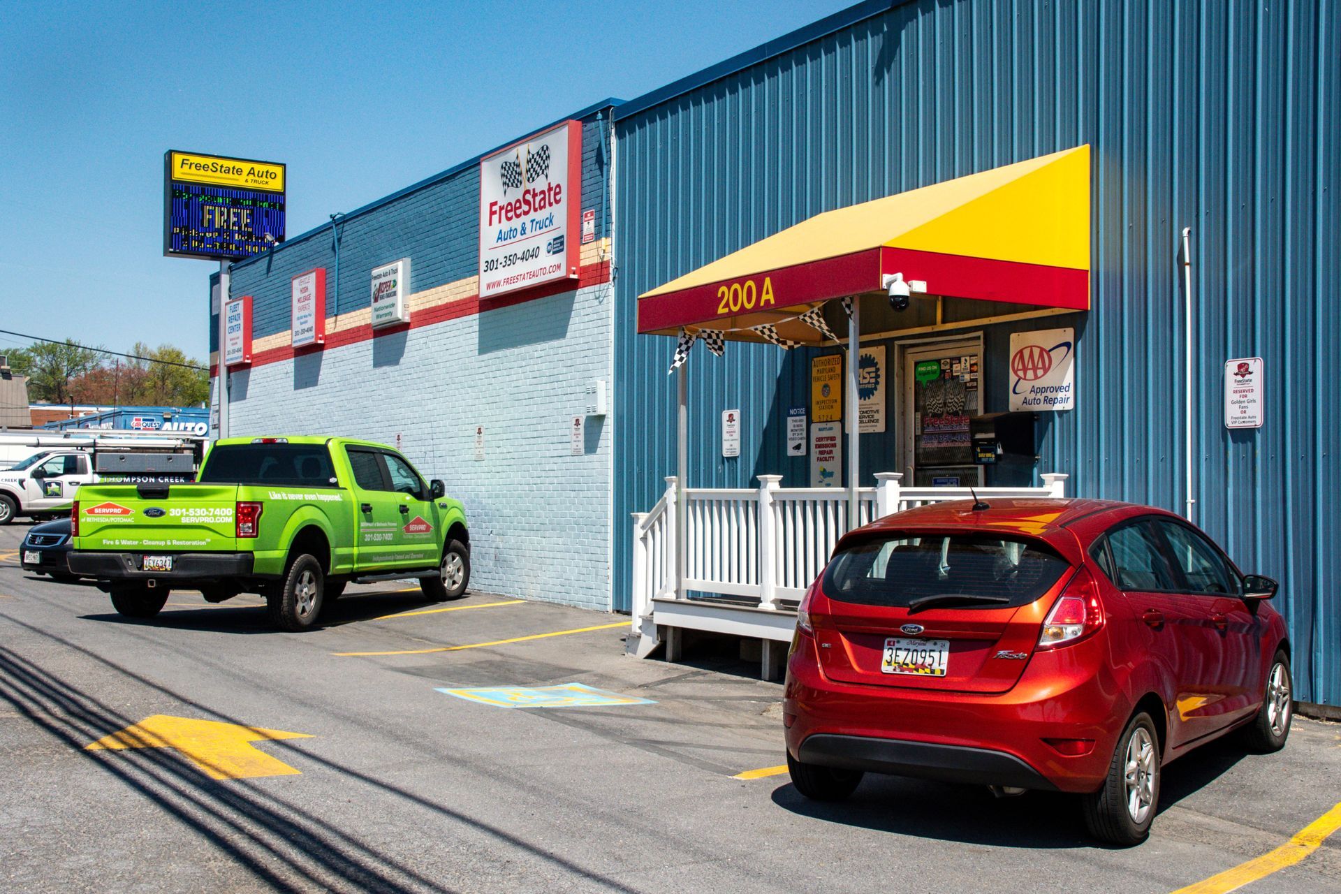 Exterior of a blue building with a yellow and red awning. Cars and a green truck are parked in front | Freestate Auto & Truck Service