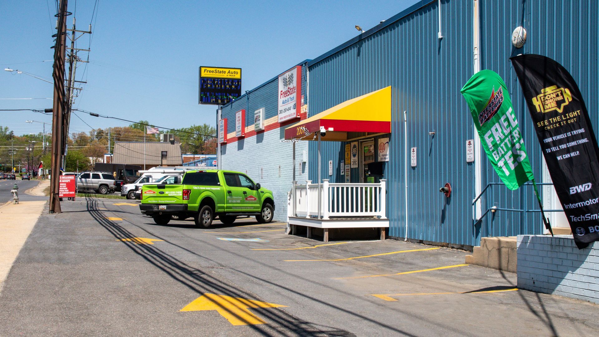 A green truck parked outside a blue building with an awning, flags, and signs on a sunny day | Freestate Auto & Truck Service