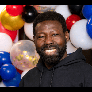 Man with a beard smiling in front of a colorful balloon display.