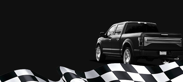 Group of people smiling, posing for a photo. They're indoors, likely a garage or shop setting with blue walls.