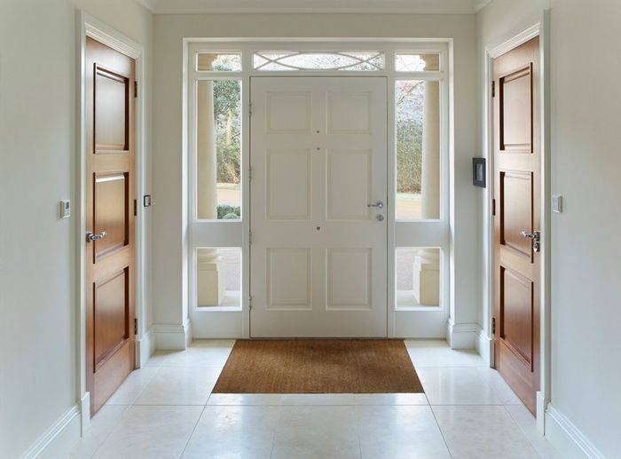 Bright entryway with white front door, sidelights, wooden side doors, and a tan doormat