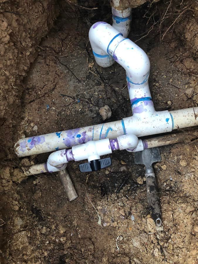 White PVC pipes and fittings in a dirt trench, including a valve, connected.