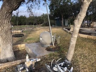 A pool filter and pump are next to a tree in a yard.