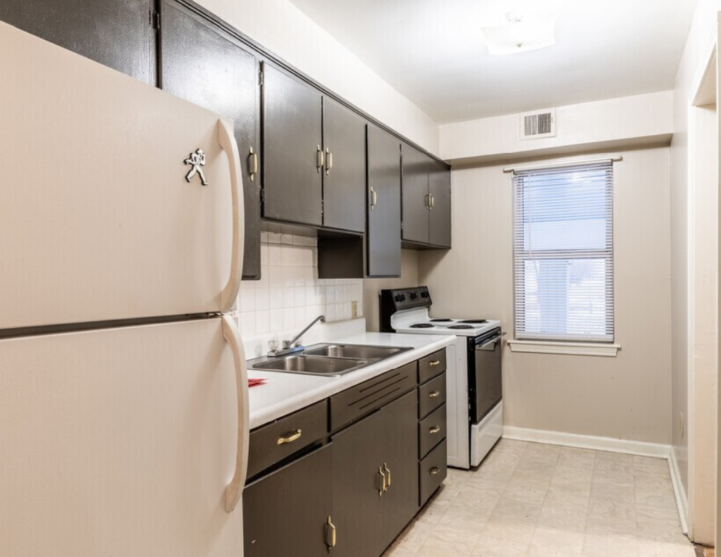 Kitchen with black cabinets, white appliances, and a window with blinds.