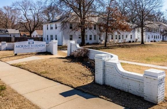 White apartment complex entrance with a sign reading "Mount Vernon Estates". Brown grass, sidewalk, and leafless trees.
