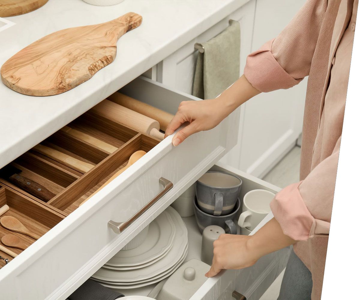 Woman opening drawers of kitchen cabinet with different dishware and utensils, closeup
