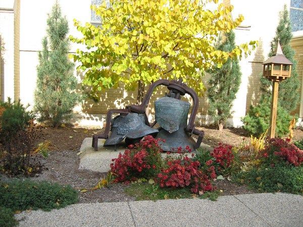 Garden sculpture beside red flowers, under a yellow-leaved tree and near a lamp post.