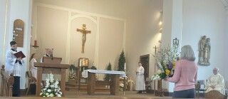 Church altar during a service, with people standing near the front and a crucifix on the wall.