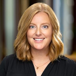 Smiling blonde woman in black blouse against a blurred indoor background