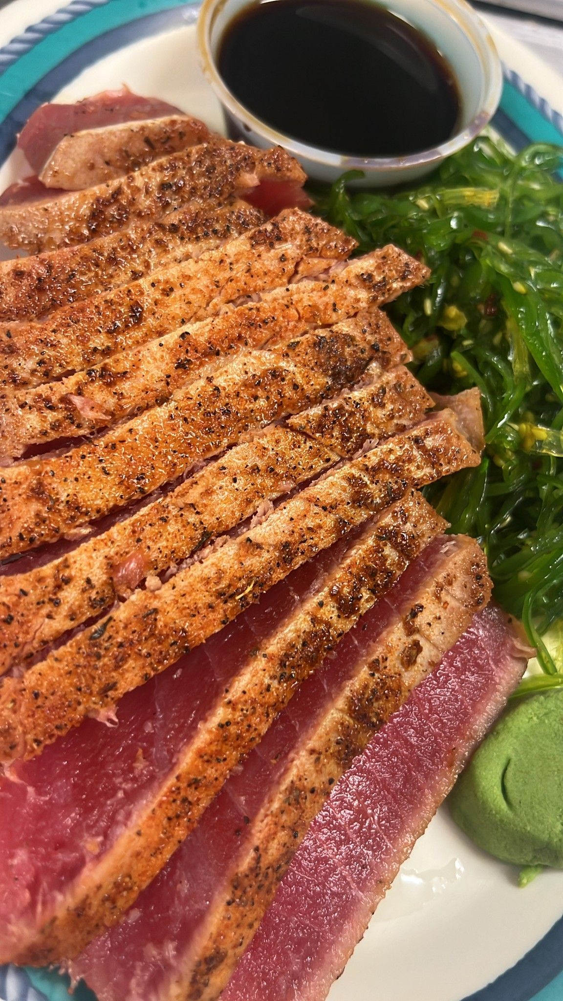 Seared tuna slices with seaweed salad, soy sauce, and wasabi on a plate. At High Tide Harry's