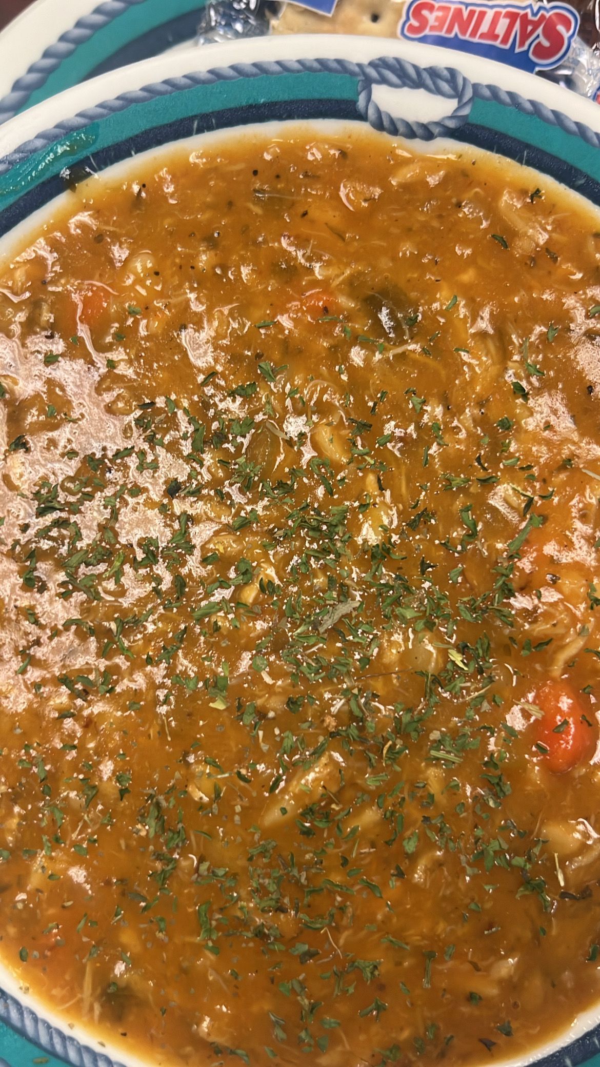 Bowl of stew, speckled with herbs, on a decorative plate with crackers visible in the background. At High Tide Harry's