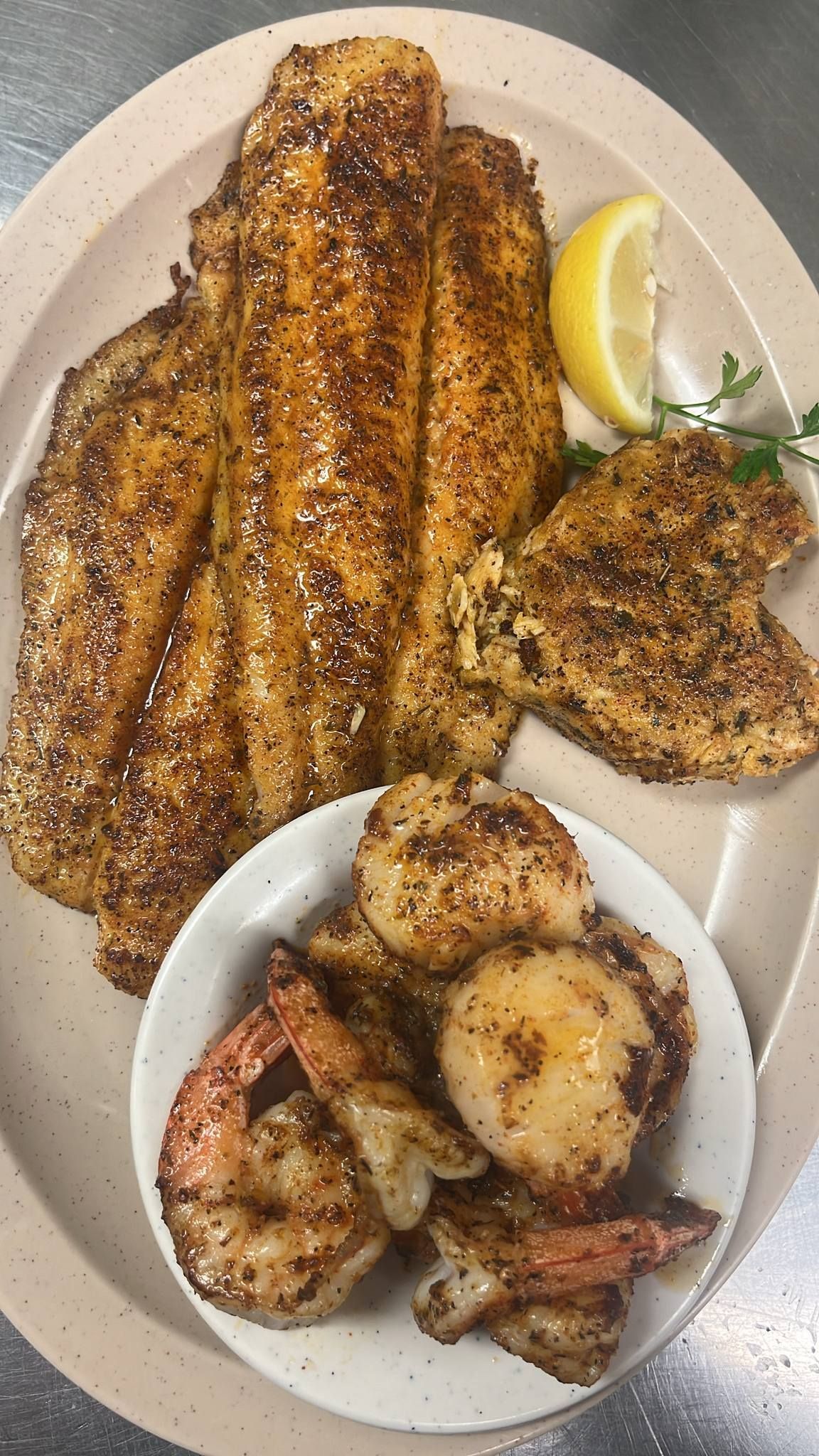Plate of seasoned seafood: fried fish fillets, shrimp, and scallops, with a lemon wedge. At High Tide Harry's