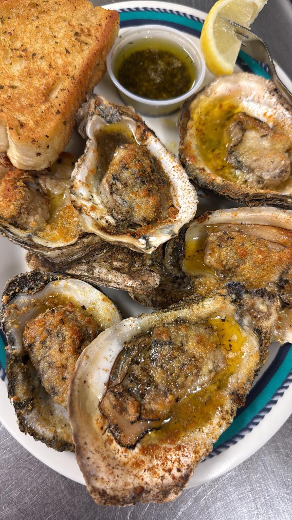 Baked oysters with lemon, garlic toast, and dipping sauce on a plate. At High Tide Harry's