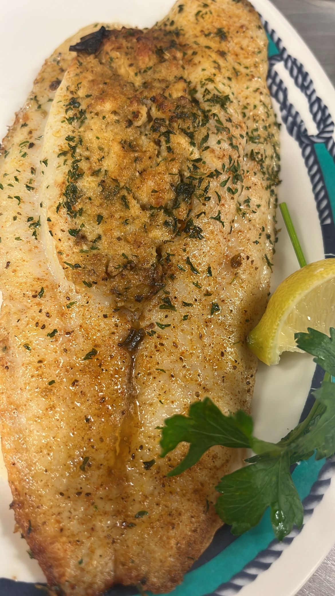 Pan-seared fish fillet on a plate with parsley and a lemon slice. At High Tide Harry's