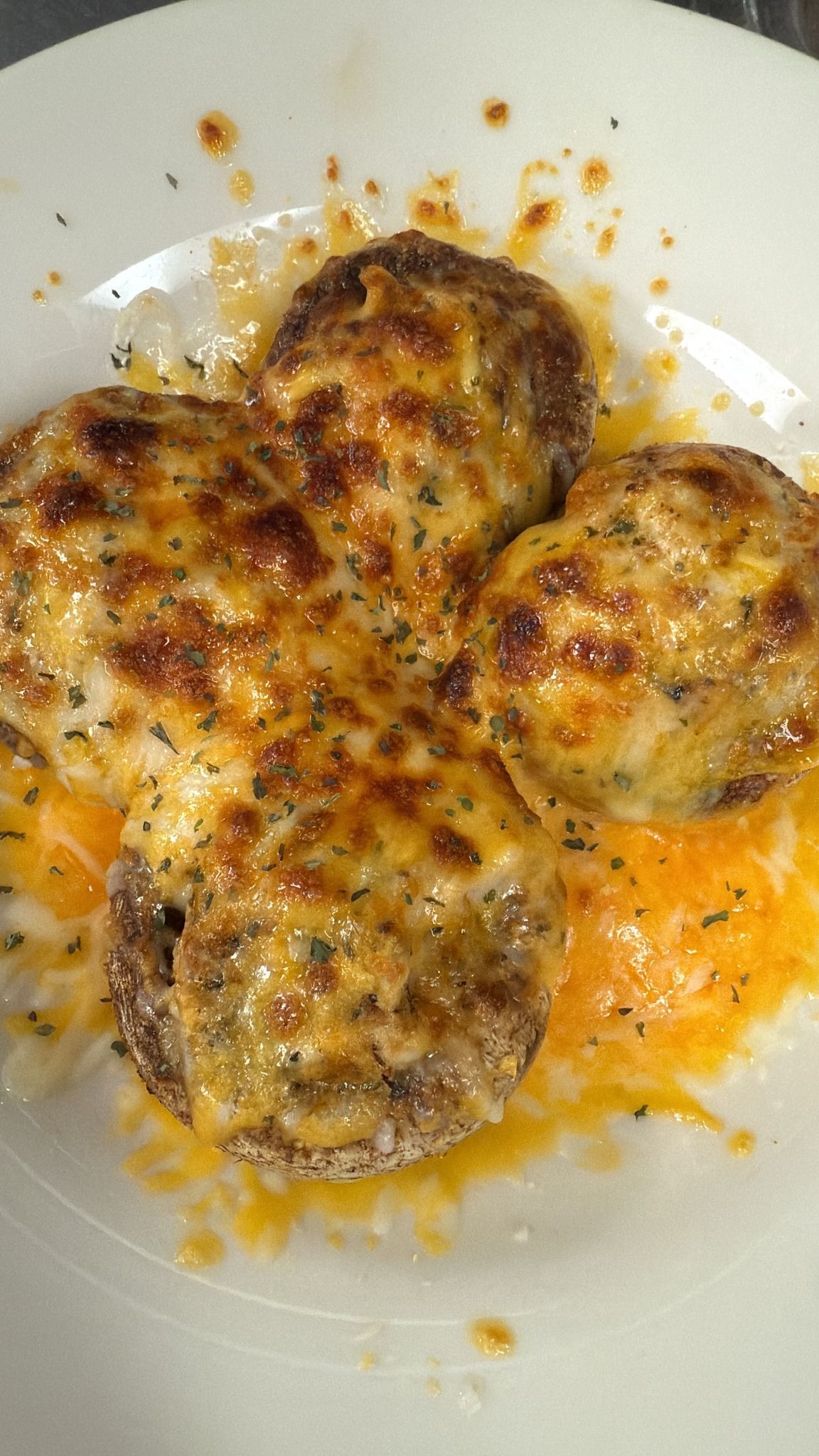 Four baked mushroom caps topped with melted cheese, on a white plate. At High Tide Harry's
