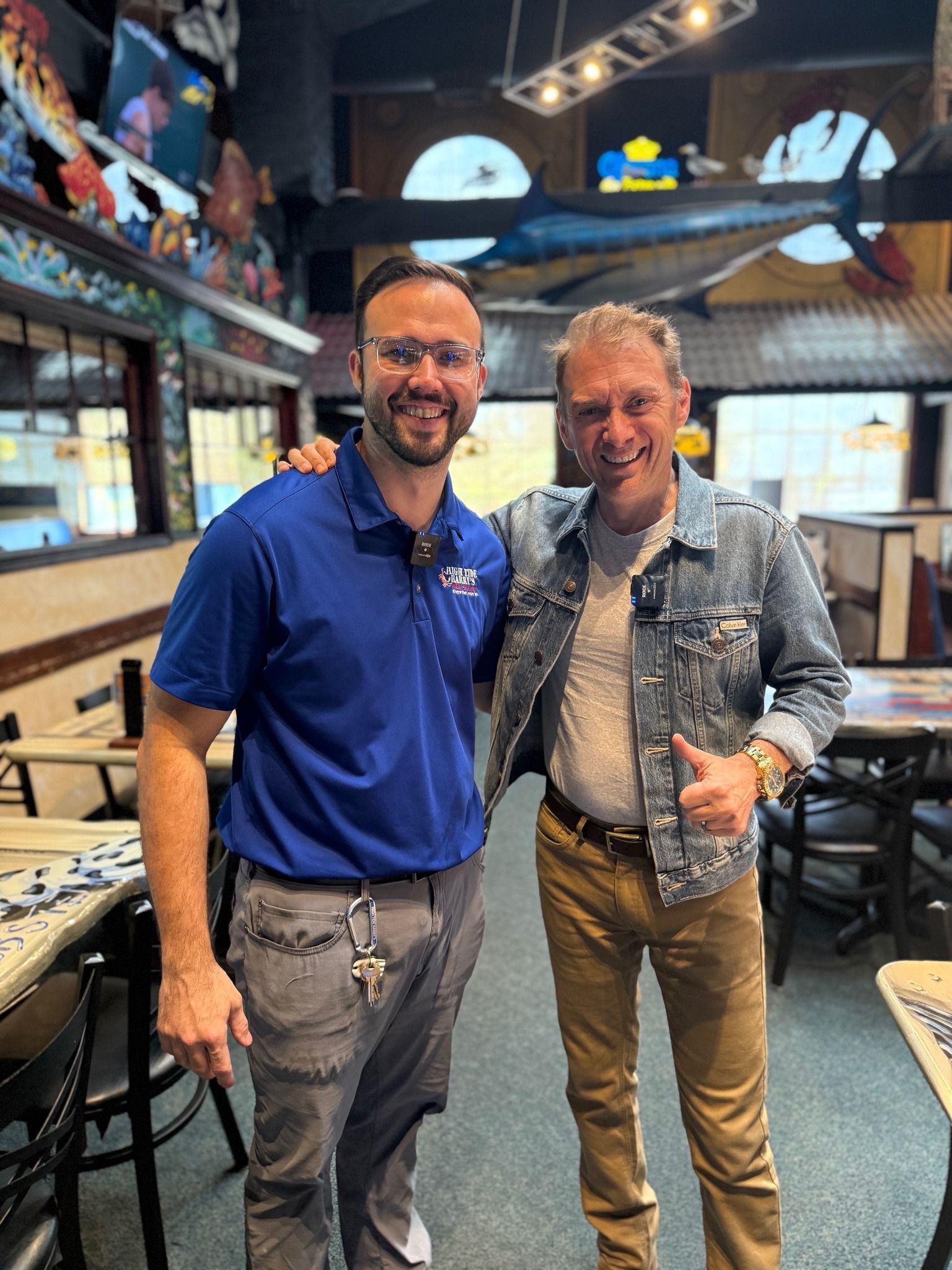 Brennan and News reporter in blue shirt and man in denim jacket pose together inside a restaurant, both smiling.