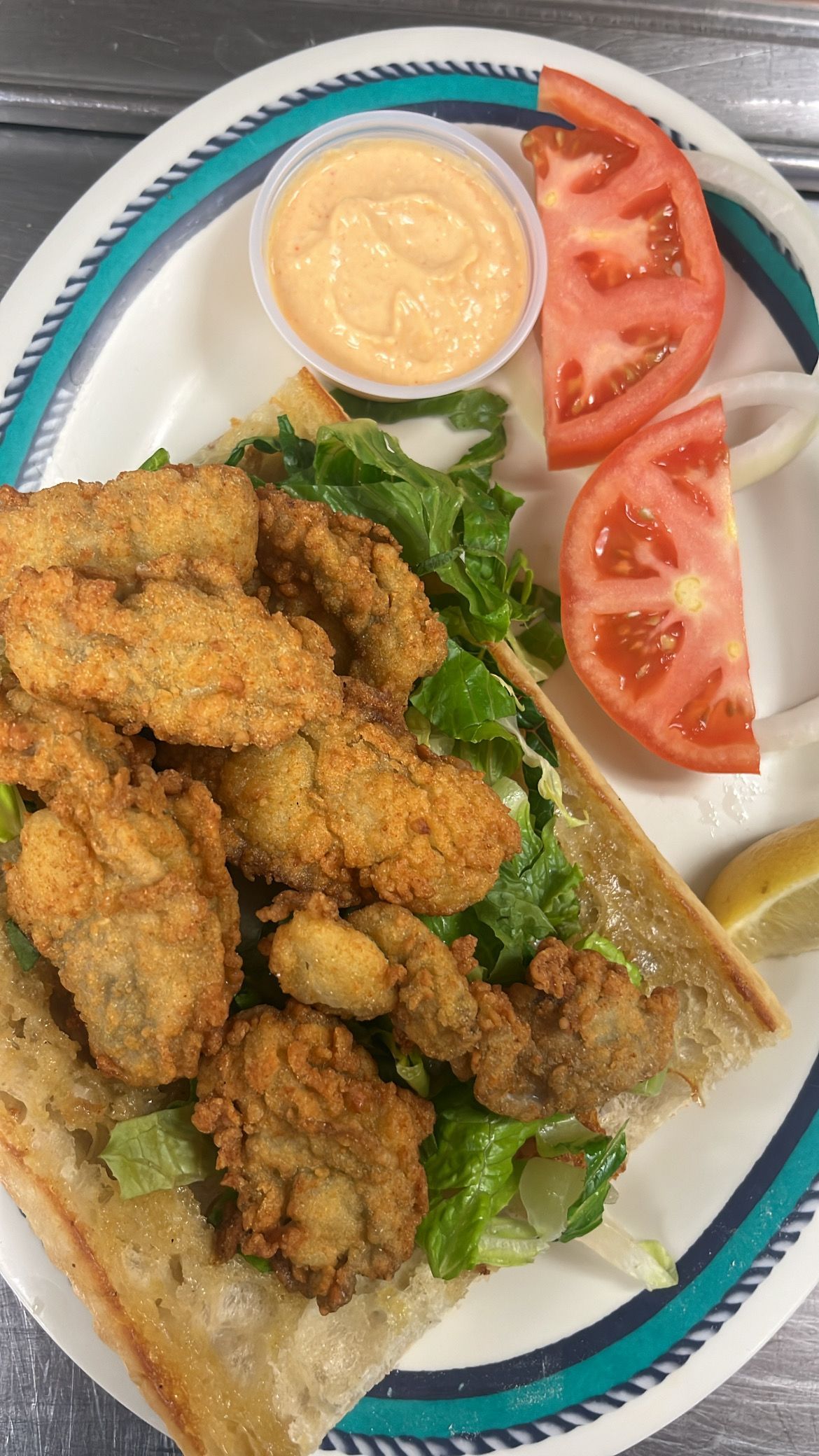 Fried oyster sandwich with lettuce, tomato, sauce, and a lemon wedge on a plate. At High Tide Harry's