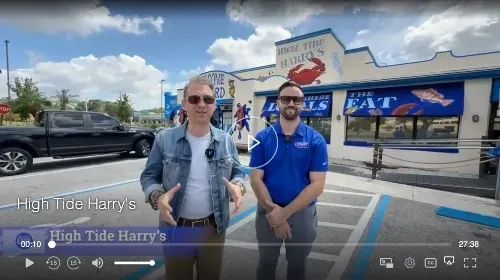 Two men standing outside High Tide Harry's restaurant. One wears a denim jacket, the other a blue polo.