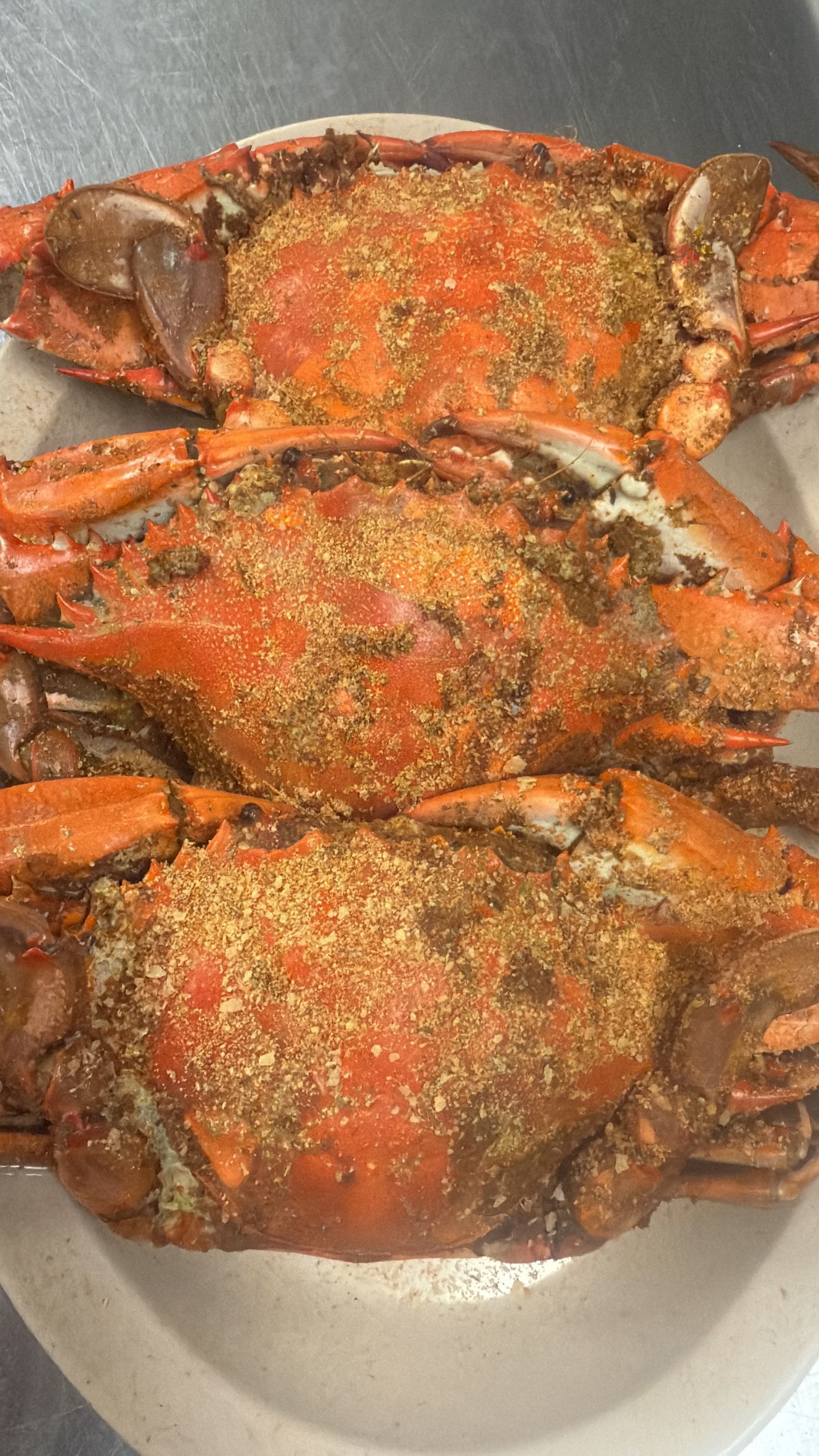 Three cooked crabs, seasoned, on a white plate. Bright orange shells, brown seasoning. At High Tide Harry's