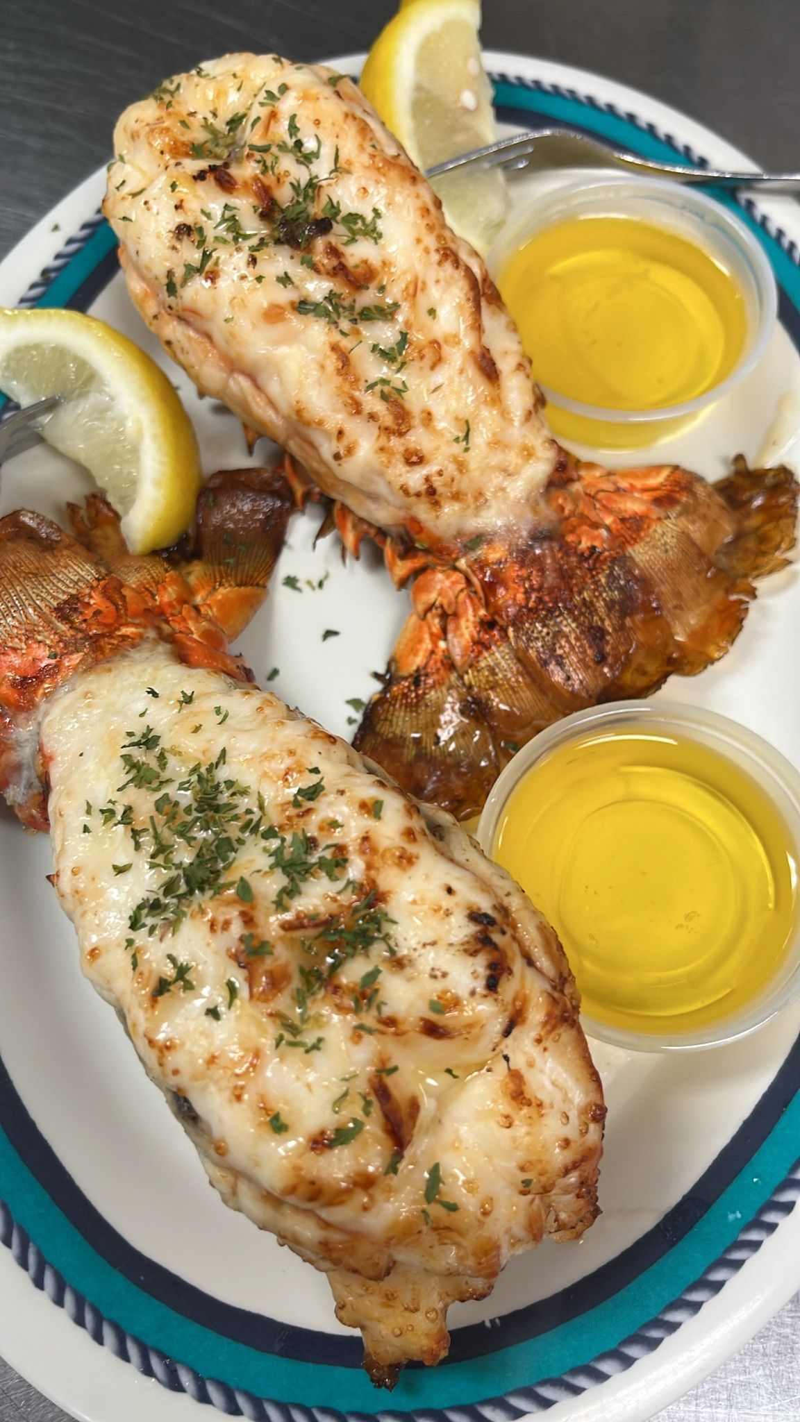 Grilled lobster tails with lemon wedges and melted butter on a plate. At High Tide Harry's