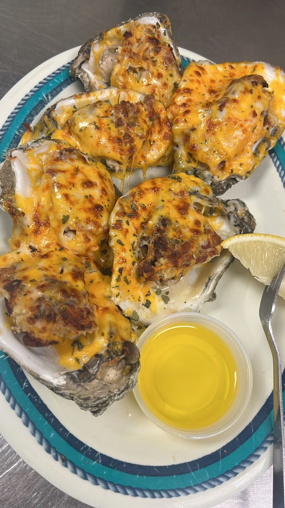 Baked oysters with melted cheese and butter, on a plate with a lemon wedge. At High Tide Harry's