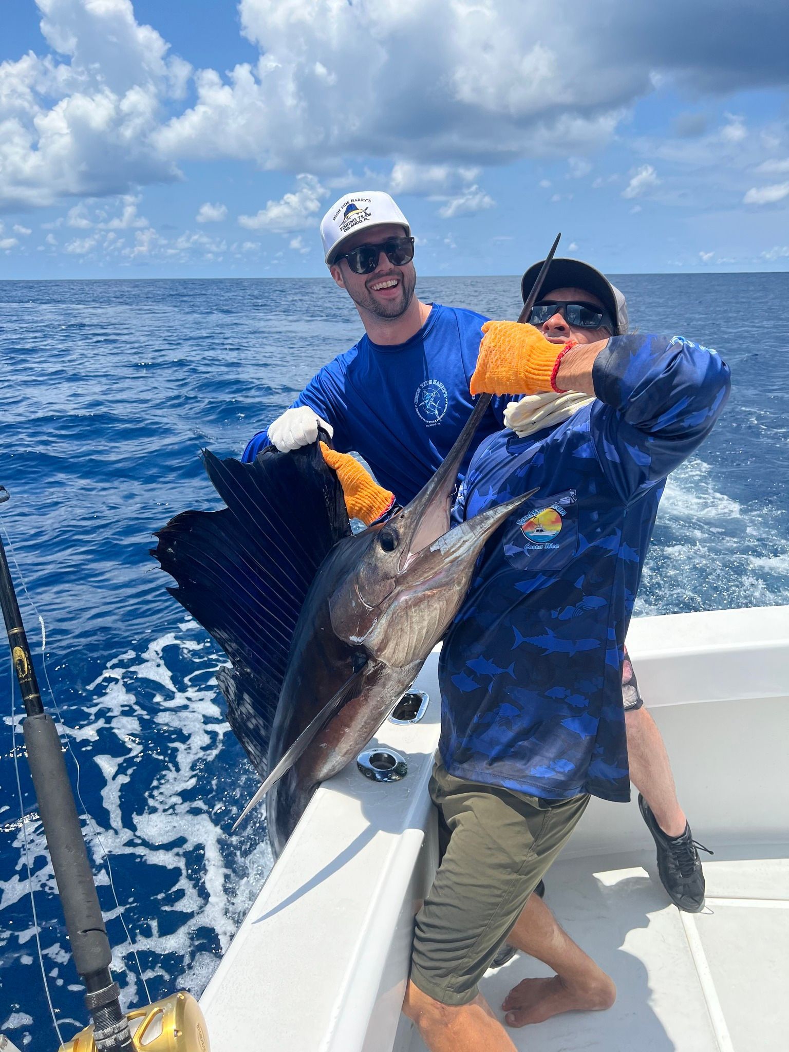 Brennan and co, from High tide Harry's on a boat, holding up a large sailfish they caught, smiling on a sunny day.