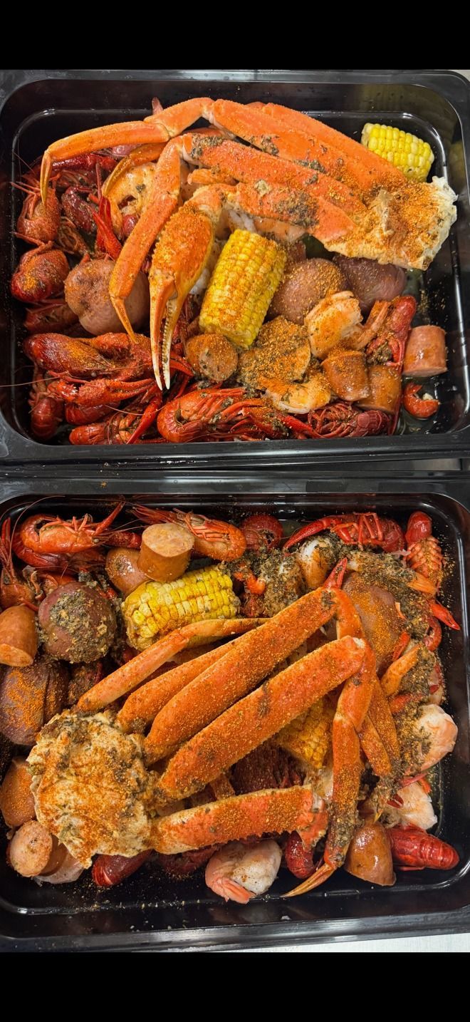 Two black containers with seafood boil: crab legs, crawfish, sausage, corn. At High Tide Harry's