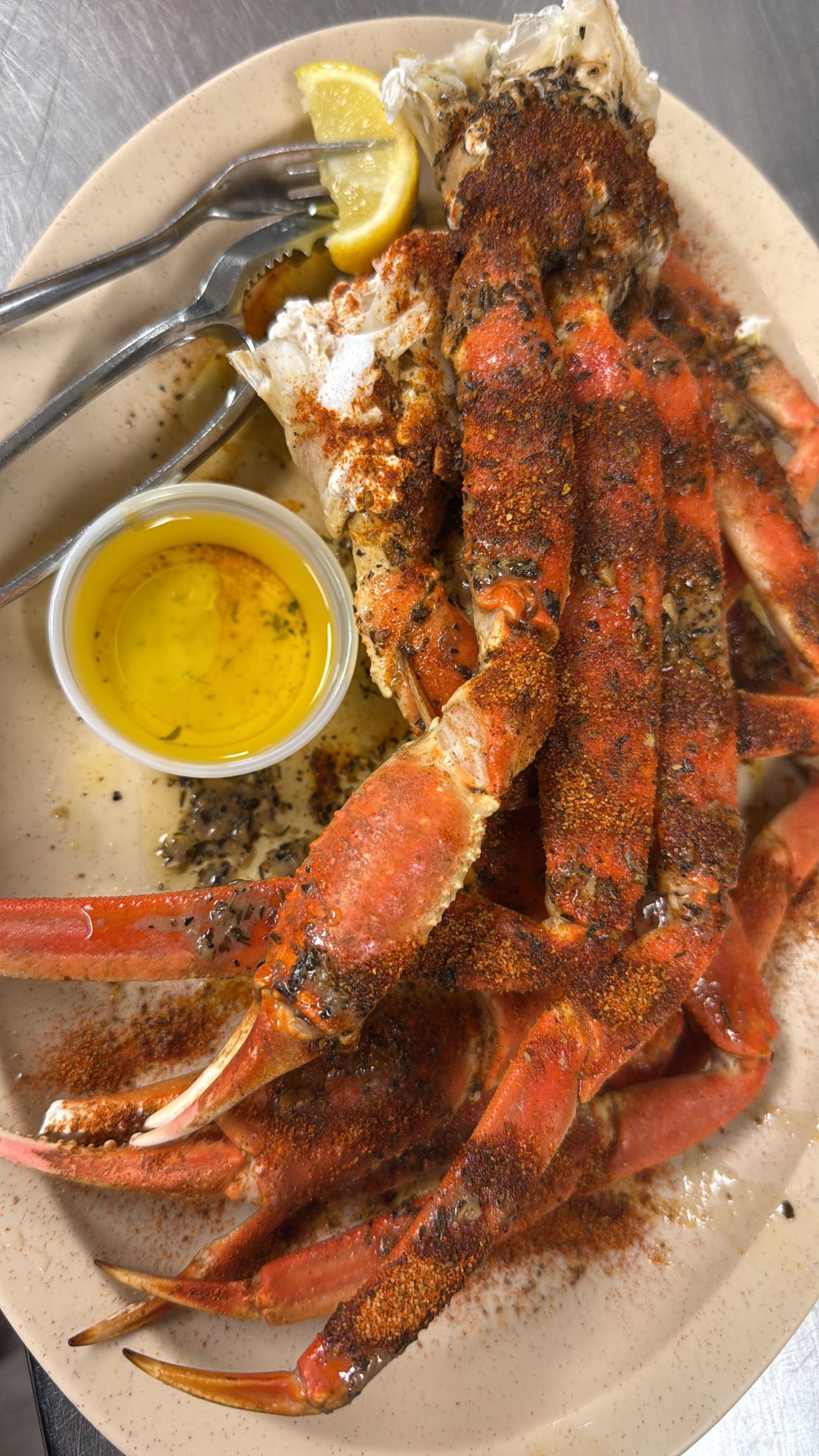 Snow crab legs with seasoning, lemon, and melted butter on a plate with utensils. At High Tide Harry's