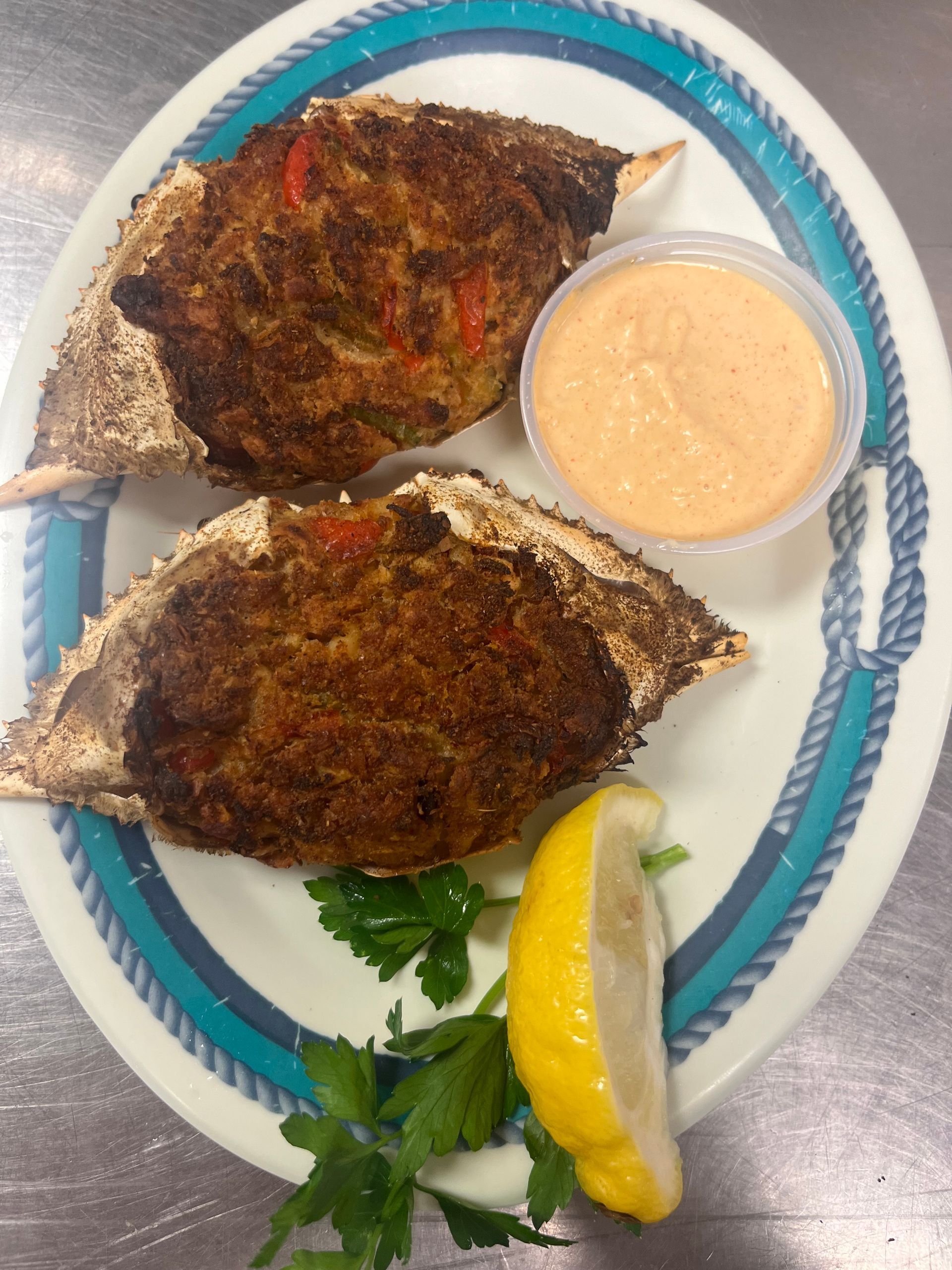 Two stuffed crab shells with sauce and lemon on a plate with nautical border. at High tide Harry's