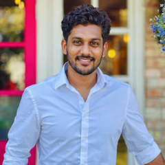 Smiling man in a light blue shirt standing outdoors near a colorful building.