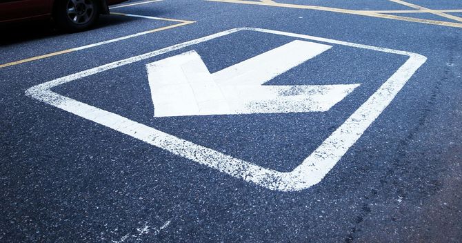 White left-turn arrow painted inside a white diamond on dark asphalt road
