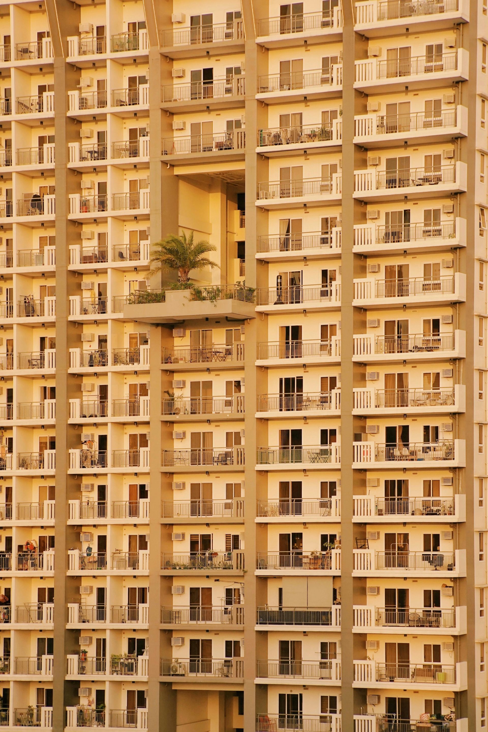 Tall beige apartment building with many balconies and a few potted plants visible on one terrace