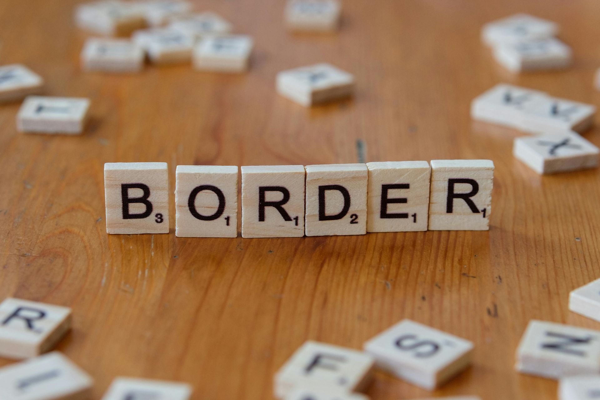 Wooden letter tiles spelling “BORDER” on a wooden table, with scattered tiles in the background