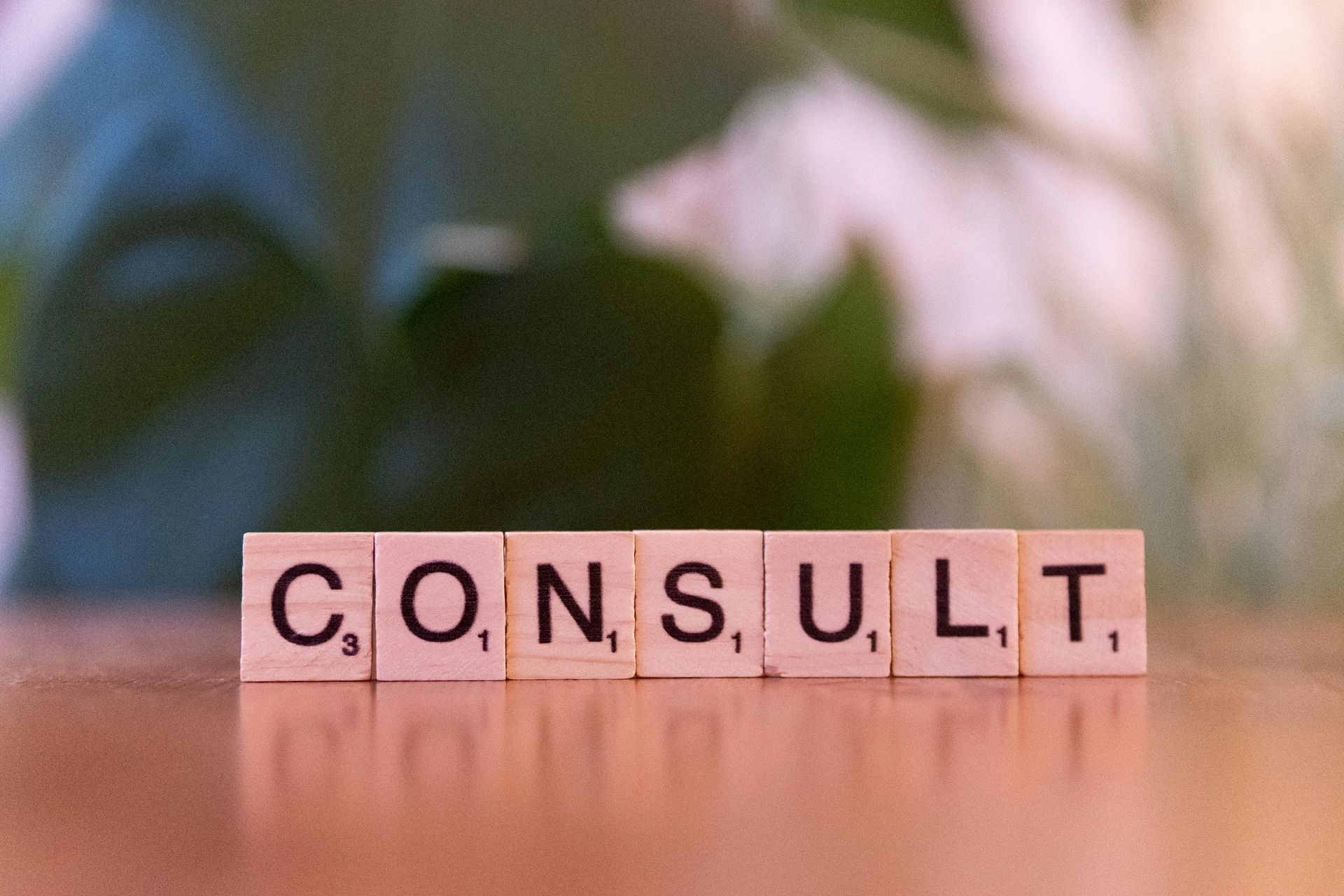 Letter blocks spelling “CONSULT” on a wooden surface with a blurred green background