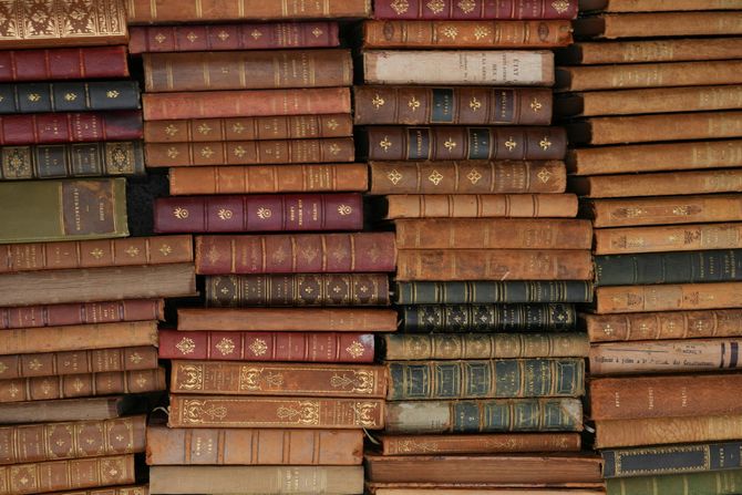 Stacked vintage books with worn brown and red leather spines on shelves