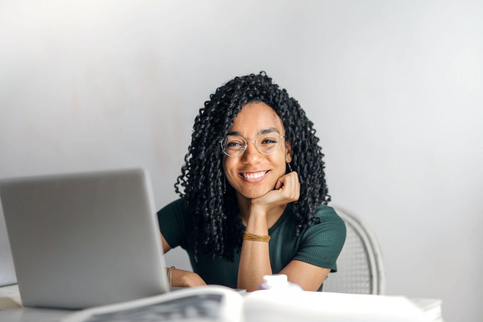 Woman smiling at a laptop on a desk, with a bright white background.