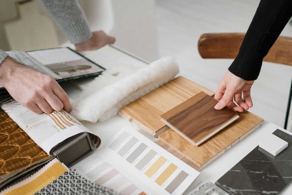 Hands reviewing wood and fabric samples on a design table with color swatches and a roller on the left