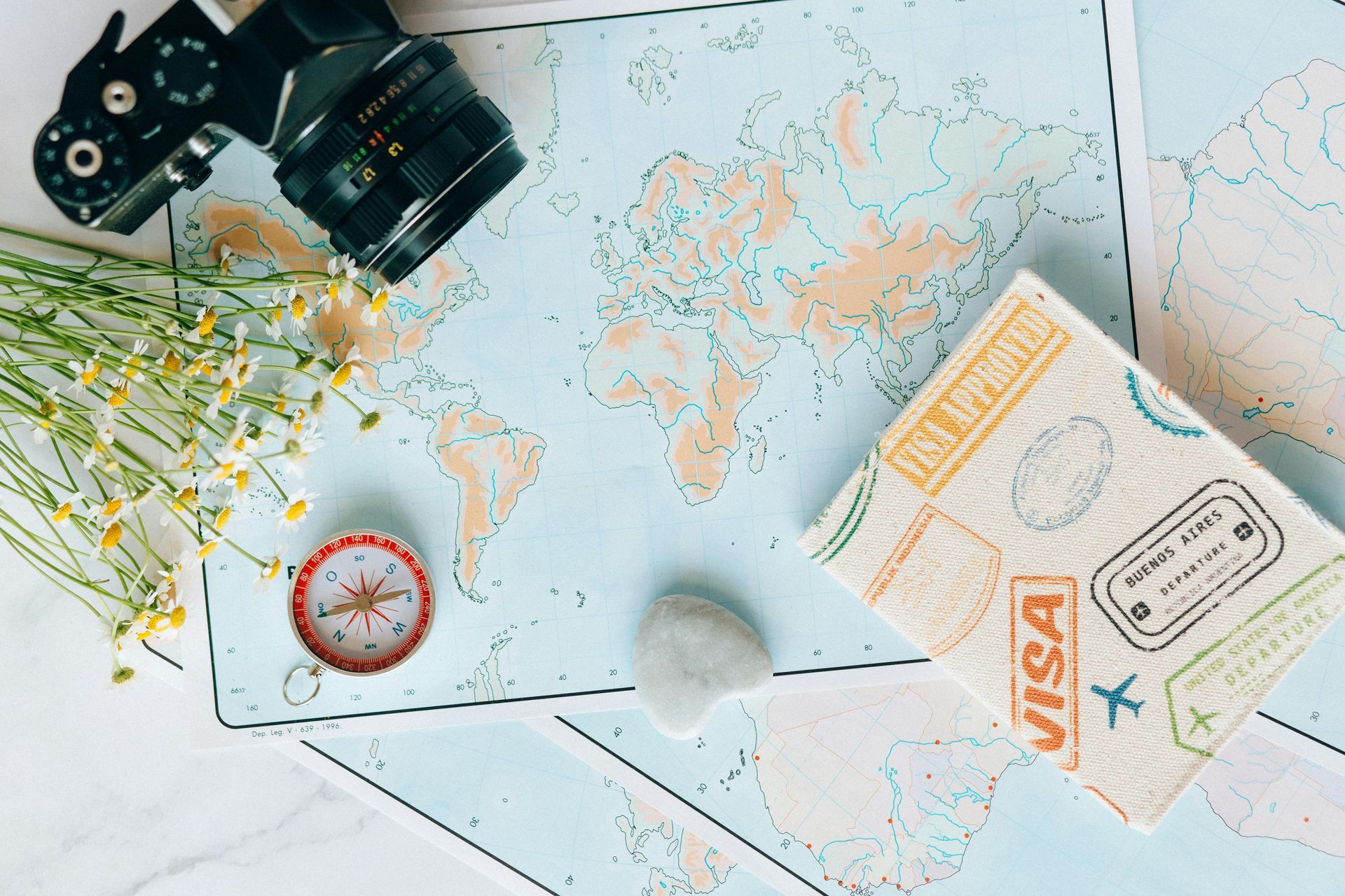 Travel flat lay with world map, camera, compass, and passport on a white desk