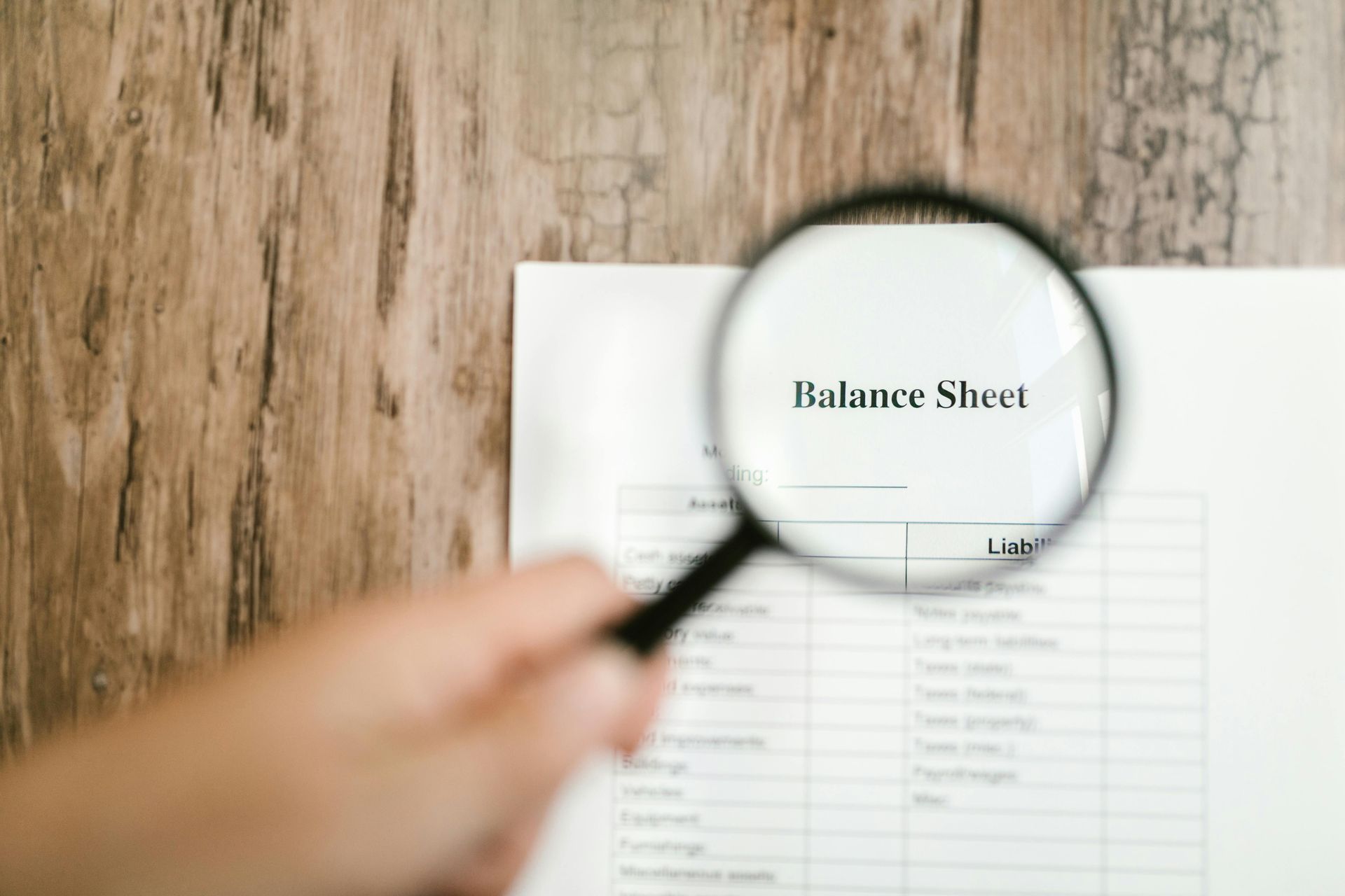 Magnifying glass over a balance sheet on a wooden desk, highlighting financial details