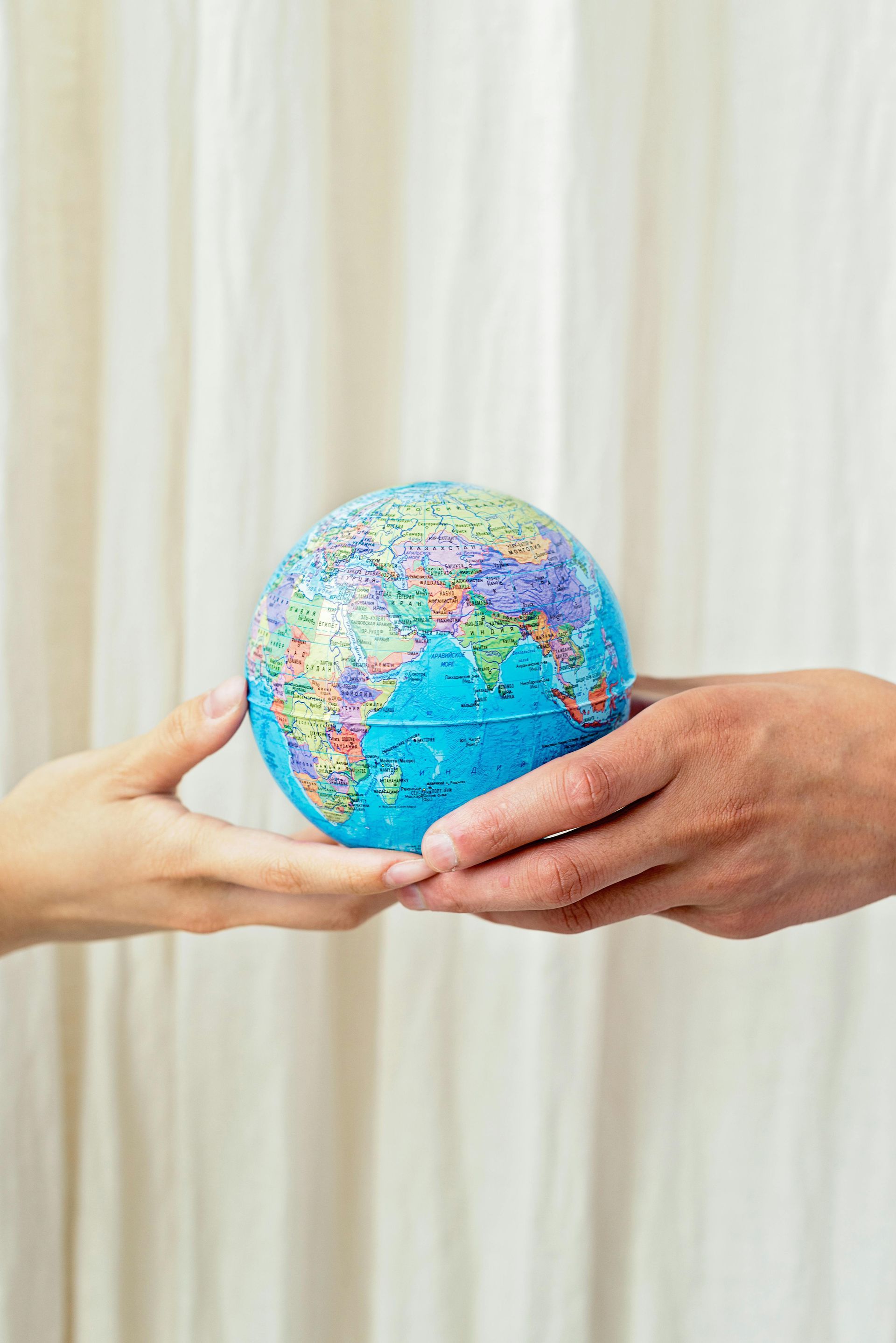 Hands passing a small globe against a light curtain background