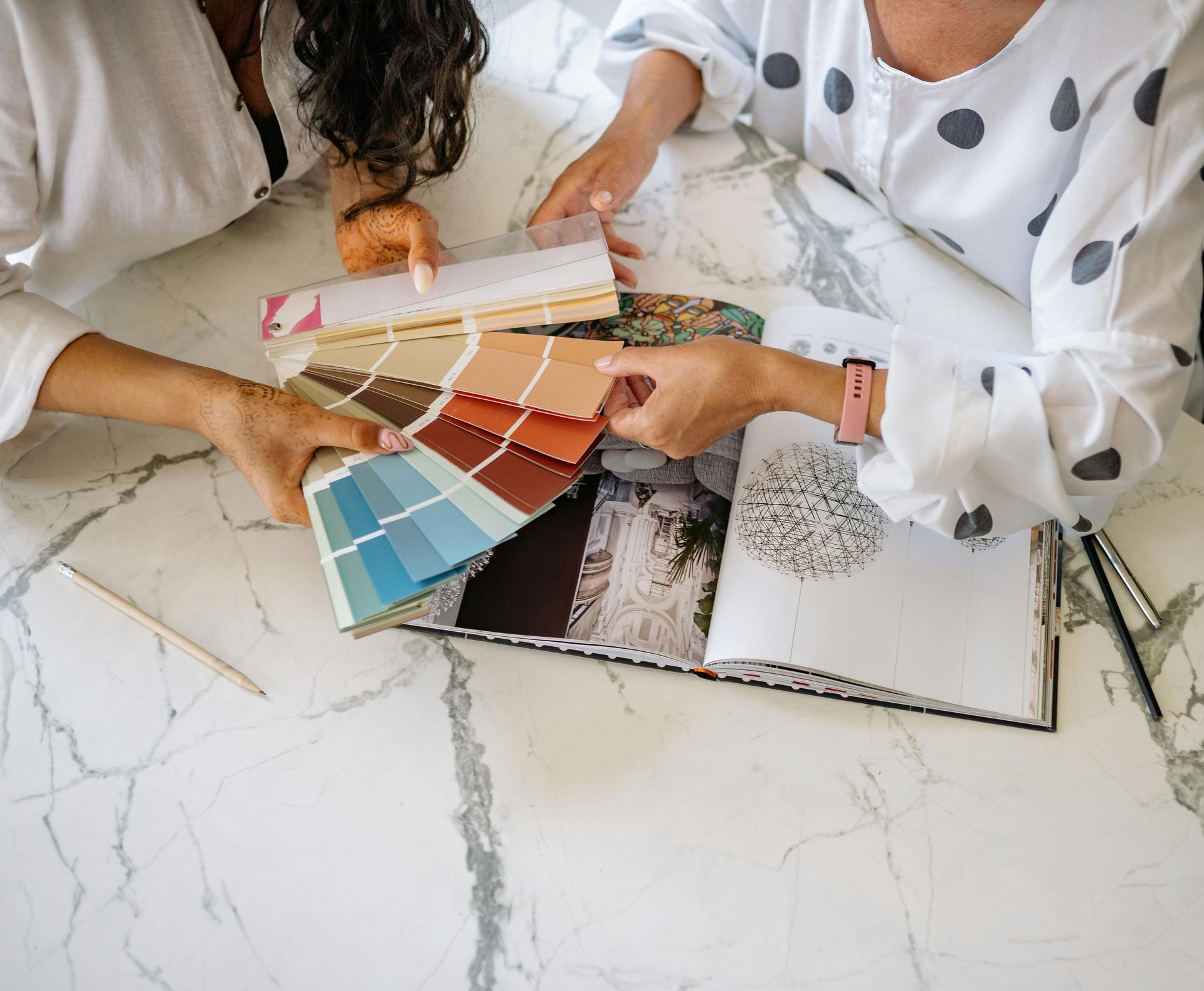 Hands selecting color swatches and fabric samples on a marble table with design books